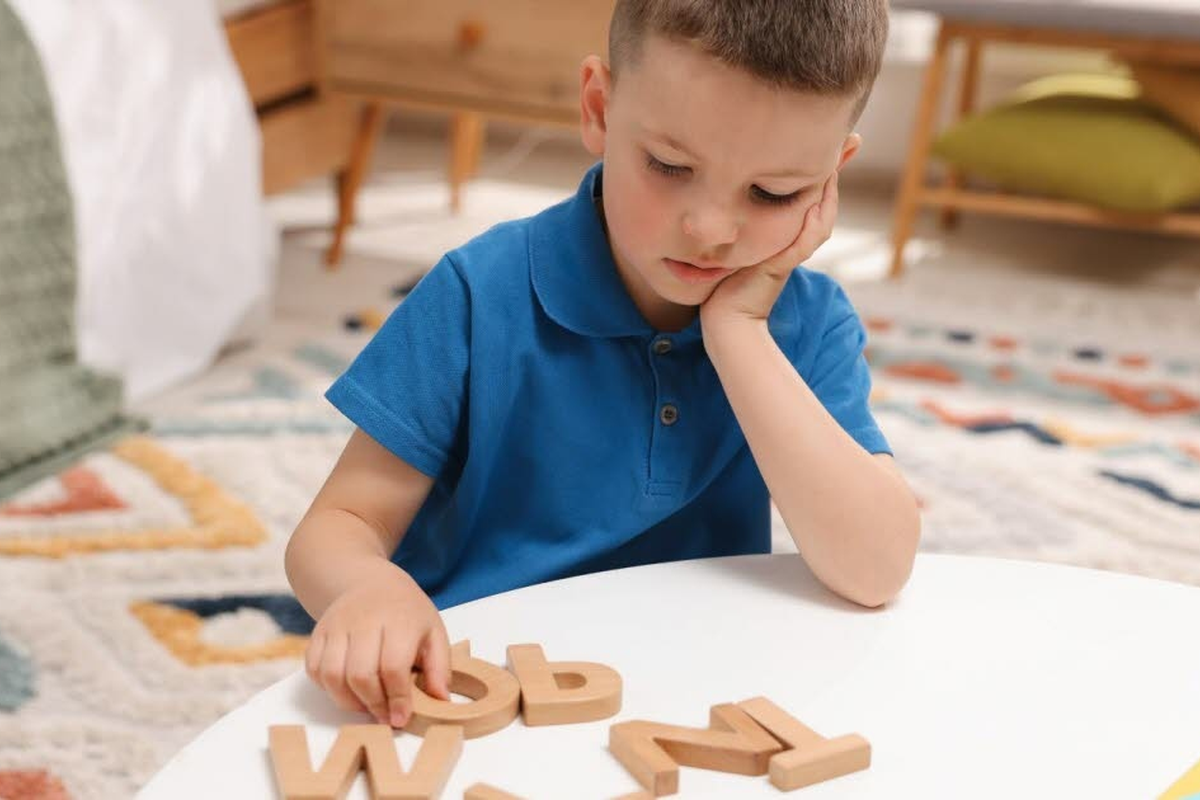 Jeune garçon songeur devant des lettres en bois, illustrant les difficultés d'apprentissage de la lecture