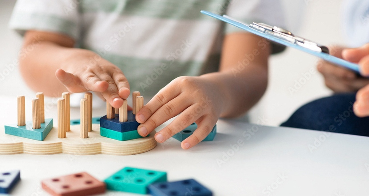 Mains d'enfant manipulant des blocs de bois pendant qu'un adulte prend des notes sur un clipboard