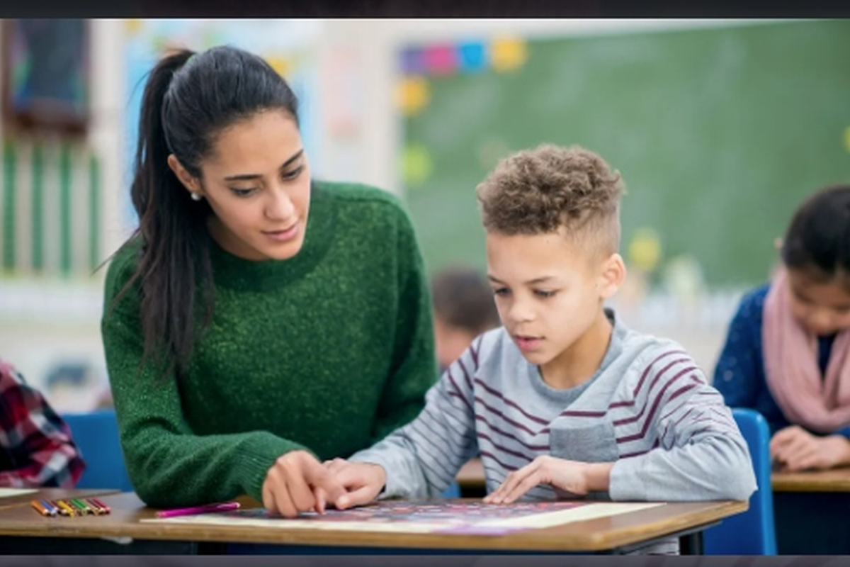 Enseignante accompagnant un jeune garçon sur un exercice en classe